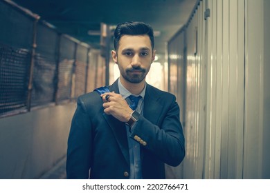 Portrait Of Young Handsome Business Man In Formal-wear Holding Necktie While Standing In The Middle Of Passage.