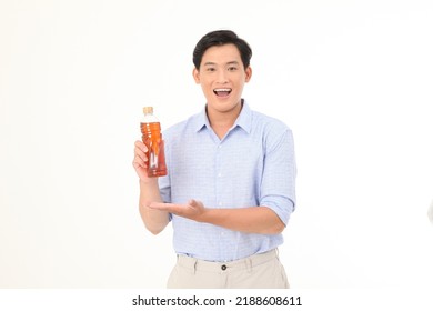 Portrait Of A Young Handsome And Cheerful Asian Adult Man, Hold A Drinking Bottle Of Tea, Excited And Full Of Energy, Isolated On White Background. Concept Of Soft Drink Advertising. 