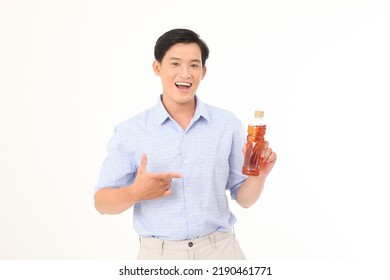 Portrait Of A Young Handsome And Cheerful Asian Adult Man, Hold A Drinking Bottle Of Tea, Excited And Full Of Energy, Isolated On White Background. Concept Of Soft Drink Advertising. 