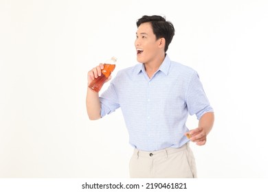 Portrait Of A Young Handsome And Cheerful Asian Adult Man, Hold A Drinking Bottle Of Tea, Excited And Full Of Energy, Isolated On White Background. Concept Of Soft Drink Advertising. 