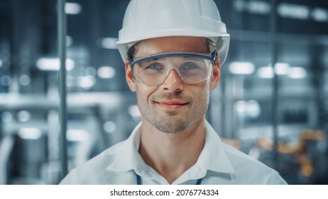 Portrait Of A Young Handsome Confident Engineer Wearing Safety Goggles And White Hard Hat In Office At Car Assembly Plant. Industrial Specialist Working On Vehicle Production In Modern Factory.