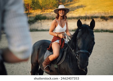 Portrait of young handsome cowgirl horseback riding at horse ranch and smiling at the cowboy in a blurry foreground. Smiling young attractive rider in western styled clothes is horseback riding. - Powered by Shutterstock