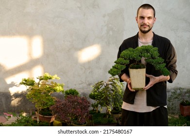 A portrait of a young handsome guy with a bonsai in his hands on the white background  - Powered by Shutterstock