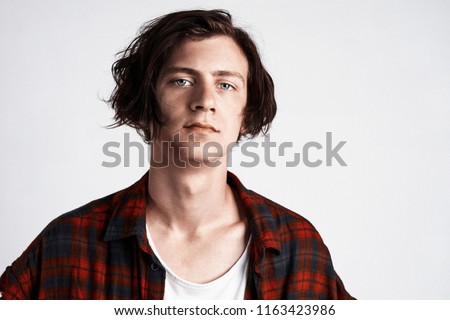 Portrait of young handsome hipster man looking at camera, wearing Scottish cell shirt, white background.
                              