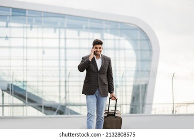 Portrait Of Young Handsome Indian Business Man Walking Outside To Station Or Airport Talking On The Phone And Carrying Suitcase.