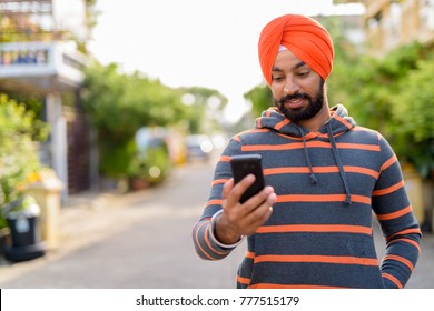 Portrait of young handsome Indian Sikh man wearing turban in the streets outdoors