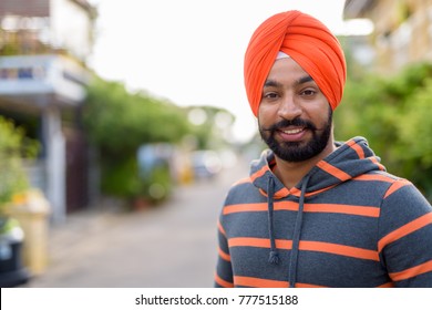 Portrait of young handsome Indian Sikh man wearing turban in the streets outdoors