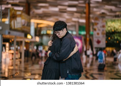 Portrait Of A Young And Handsome Korean Asian Man In A Casual Outfit And Jacket Hugging A Woman At The Airport. He Looks Sad That He Is To Be Parted With His Girlfriend. 