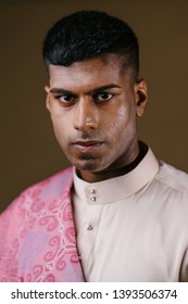 Portrait Of A Young And Handsome Malaysian Indian Muslim Man In A Cream Colored Traditional Baju Melayu Outfit With A Striking Pink Sash. He Is Dressed Festively To Go Visiting For Raya. 