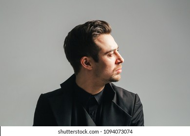 Portrait Of A Young Handsome Man In A Black Suit, Seriously Looking To The Side, Against Plain Studio Background