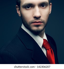 Portrait of a young handsome man (businessman) in black classic suit with trendy red tie. Close up. Studio shot