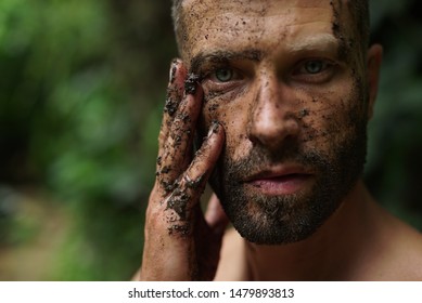 Portrait young handsome man with dirty hand and face looks at camera in wild forest