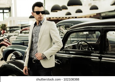 Portrait Of A Young Handsome Man, Model Of Fashion, Wearing Jacket And Shirt With Old Cars