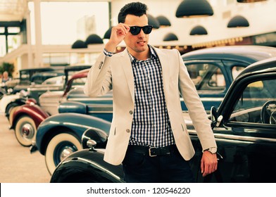 Portrait Of A Young Handsome Man, Model Of Fashion, Wearing Jacket And Shirt With Old Cars