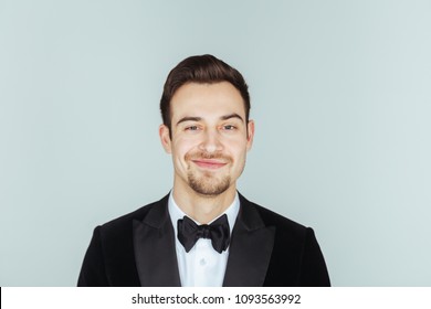 Portrait Of A Young Handsome Man In A Tuxedo,  Seriously Looking At The Camera, Against Plain Studio Background.