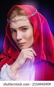 Portrait Of A Young Handsome Prince Of Elves Wearing A Red Velvet Cloak And A Crown. Studio Portrait On A Black Background. Fairy Tale, Magic. Fantasy.