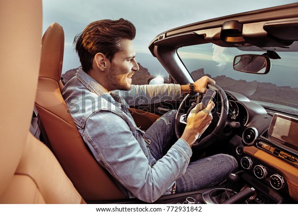 Portrait of a young handsome, rich man driving his\
convertible car