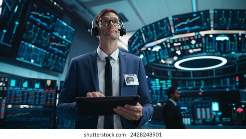 Portrait of a Young Handsome Stock Exchange Broker Using Tablet Computer, Researching Real-Time Stocks Data, Analyzing Commodities and Exchange Market Charts. Professional Investment Agent in Office