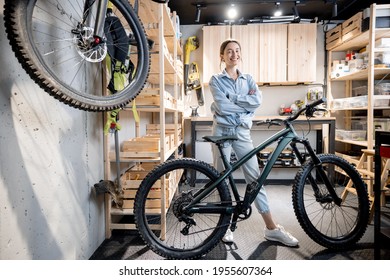 Portrait of a young handywoman standing with a bicycle in the workshop or garage at home. Bicycle repairing and diy concept - Powered by Shutterstock