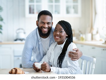 Portrait Of Young Happy African American Couple Posing At Table In Kitchen, Millennial African American Spouses Enjoying Coffee With Croissants For Breakfast At Home And Smiling At Camera, Free Space
