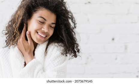 Portrait of young happy afro american woman in bathrobe touching her pure clean skin on face, closed eyes, smiling wide, standing on copy space background. Skincare, dermatology, cosmetology concept - Shutterstock ID 2073679145