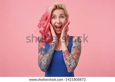 Portrait of young happy amazed nice pink haired lady, with palms on cheeks, her boyfriend proposed to her, looks at the camera with wide open mouth, feels happines, stands over pink background.