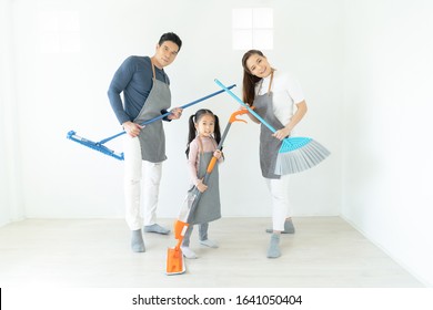 Portrait Of Young Happy Asian Family Cleaning Home And Playing With Mop And Broom In Living Room. With Fun And Looking At Camera.  People, Love, Family, Housekeeping And Home Cleaning Concept.