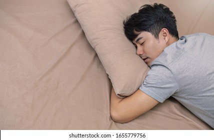 Portrait Of Young Happy Asian Man With Attractive Smile Sleeping Laying Indoor Apartment Bed Room . Asian Man Sleep Tight In Bed With Copy Space. Healthy Care Good Night Sleep Concept