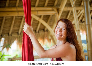 Portrait Of Young Happy And Beautiful Red Hair Woman At Aerial Dancing Workshop Learning Aero Dance Holding Silk Fabric Smiling Cheerful In Tropical Wooden Hut