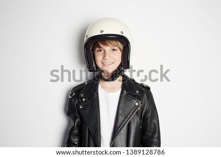 Portrait of Young happy beautiful teen kid in black leather jacket and white moto helmet smiling on white background