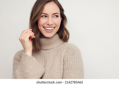 Portrait of young happy beautiful woman smiling and standing isolated on white background in a warm sweater. Young female girl with a perfect smile looking right.