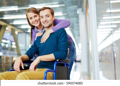 Portrait of young happy couple: pretty girl hugging her smiling handicapped boyfriend in wheelchair - Powered by Shutterstock