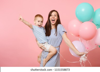 Portrait Of Young Happy Family, Mother Keep In Arms, Have Fun, Hug Child Kid Son Baby Boy, Celebrating Birthday Holiday Party On Pink Background With Colorful Air Balloons. Sincere Emotions Concept