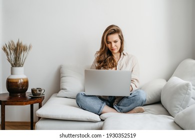 Portrait of a young happy female freelancer sitting on the couch and working on project, watching movie on laptop, studying, blogging, resting and chatting online. High quality photo