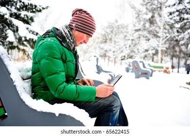Portrait of young happy handsome man working on his laptop outdoor sitting on bench in winter park