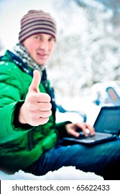 Portrait of young happy handsome man working on his laptop outdoor sitting on bench in winter park