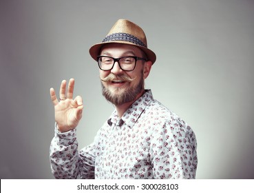 Portrait of young happy hipster showing cool gesture, isolated on grey background
