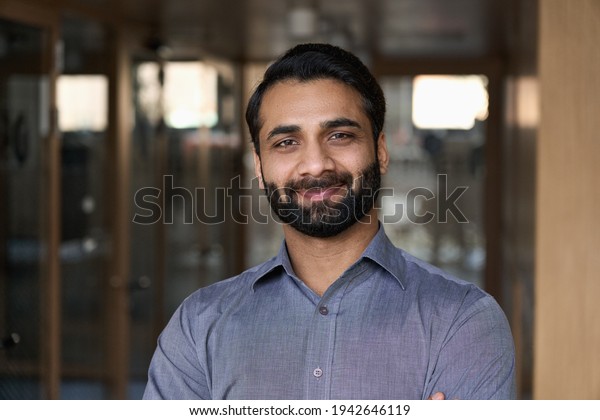Portrait of young happy indian business man
executive looking at camera. Eastern male professional teacher,
smiling ethnic bearded entrepreneur or manager posing in office,
close up face
headshot.