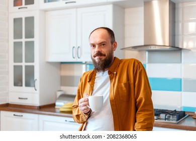 Portrait young happy man drinking coffee or tea in kitchen at home interior. Bald bearded 30s man enjoys morning routine in kitchen apartment.  - Powered by Shutterstock