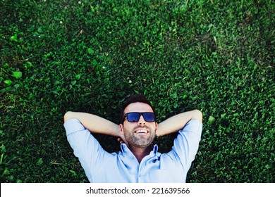 Portrait of a young happy man relaxing on the grass with his hands under the head - Shutterstock ID 221639566