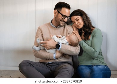 Portrait of young happy man and woman holding newborn cute babe dressed in white unisex clothing. - Shutterstock ID 2337570819