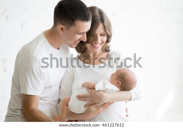 新生児のかわいい赤ちゃんを持つ幸せな若い男性と女性のポートレートで 白いユニセックスの服を着ています 白人の笑顔を持つ父親と母親が 優しく生まれ変わった子どもを抱きしめている 幸せな家族のコンセプト の写真素材 今すぐ編集