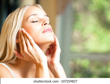 Portrait of young happy smiling cheerful beautiful blond woman applying creme, at home, with copyspace