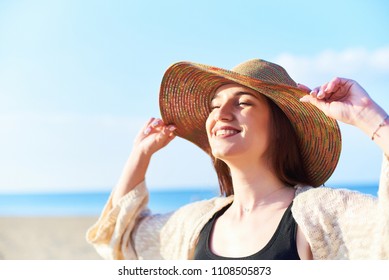 Portrait Of Young Happy Woman With Closed Eyes Wearing Straw Hat Relaxing And Enjoying The Sun On The Beach. Close-up Face Of Beautiful Young Woman Feeling Good At Seaside.