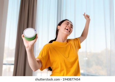 Portrait Of A Young Happy Woman Dancing And Holding A Portable Smart Speaker That Plays Music. The Concept Of Modern Gadgets.