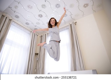 Portrait of a young happy woman jumping on the bed 