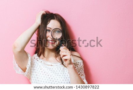 Portrait of young happy woman looking  a magnifying glass, isolated over pink background
