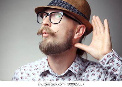 Portrait of young hipster cupping hand behind ear - can't hear you concept