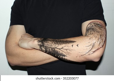 Portrait of young hipster man with tattooes on his hand. Tattoo design in the form eagle and dark forest.
