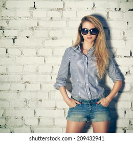Portrait of Young Hipster Woman with Hands in Pockets on White Brick Wall Background. Trendy Urban Fashion Concept. Toned Instagram Styled Photo.
